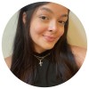 Fotografia de uma jovem mulher de cabelo longo e escuro, sorridente, vestida com uma blusa preta e um colar com pendente de cruz.
